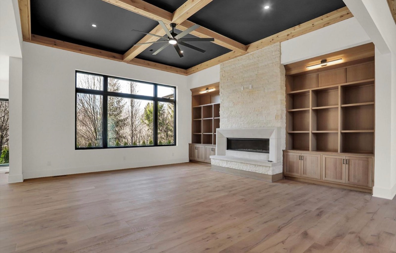 Great room with beamed charcoal ceiling, stone fireplace and white oak built in shelving